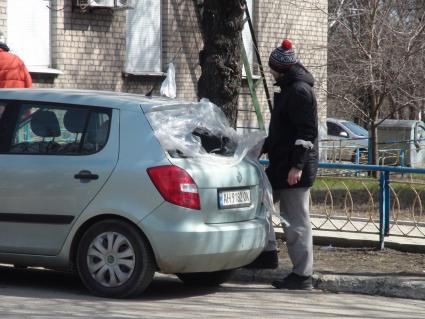 Донецкая область. Пригород Мариуполя. п. Володарское. Местный житель у своего автомобиля с выбитыми стеклами, закрытыми полиэтиленовой пленкой.