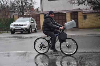 Украина. г.Мариуполь. Местный житель с пустой баклашкой для воды едет на велосипеде.