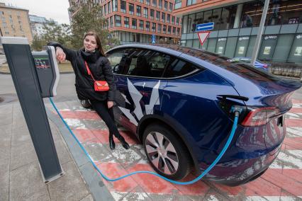 Москва. Девушка во время зарядки электрокара Tesla Model Y оператора каршеринга `Ситидрайв`.