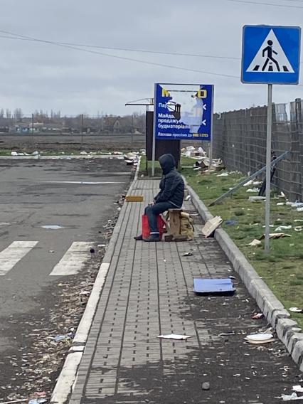 Украина. г.Мариуполь. Мужчина с сумкой сидит у забора рядом с гиипермаркетом, где выдают гуманитарную помощь.