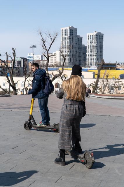 Владивосток. Молодые люди катаются на электросамокате.