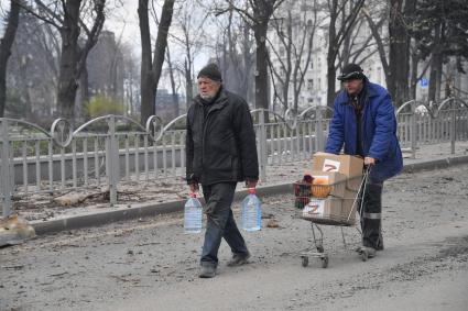 Украина. г.Мариуполь. Мужчины несут воду и гуманитарную помощь на тележке.