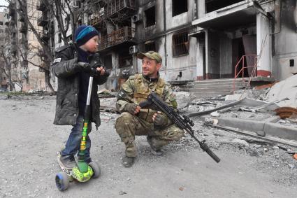 Украина. г.Мариуполь. Мальчик и военнослужащий рядом с жилым домом, разрушенным в результате обстрелов.