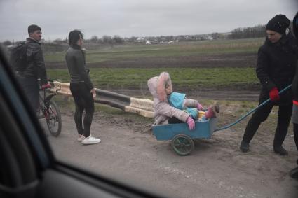 Украина. г.Мариуполь. Женщина везет девочку в тележке по обочине дороги.