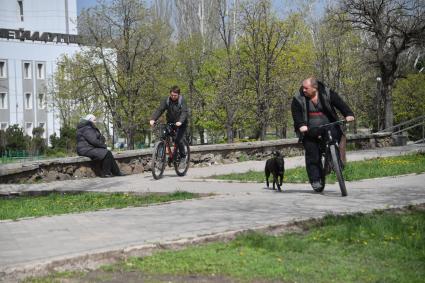 Мариуполь, Донецкая народная республика. Мужчины едут на велосипедах по улице города.