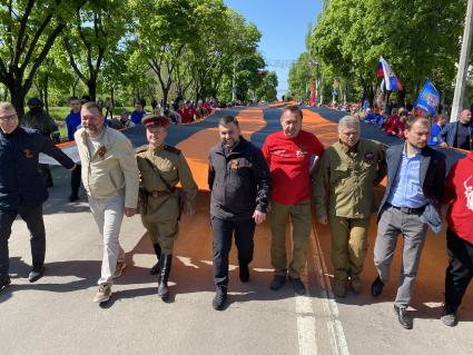 Донецкая область. г.Мариуполь. Глава ДНР Денис Пушилин (третий слева), руководитель администрации Мариуполя Константин Иващенко (третий справа), волонтеры российских общественных движений и горожане несут 300-метровую георгиевскую ленту во время шествия, в честь празднования 77-й годовщины Победы в Великой Отечественной войне.