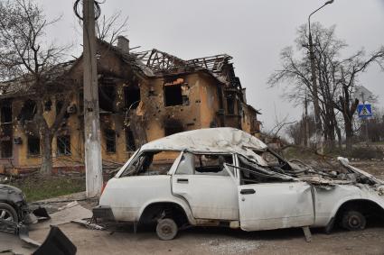 Донецкая область. г.Мариуполь. Разбитый автомобиль без колес рядом с домом, разрушенным в результате боевых действий.