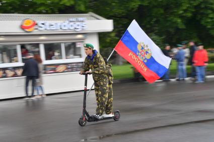 Москва. Молодые люди катаются на электросамокате с флагом РФ во время празднования Дня пограничника в Парке Горького.