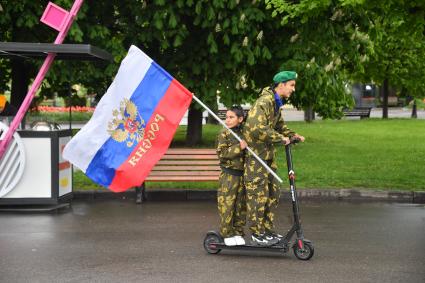 Москва. Молодые люди катаются на электросамокате с флагом РФ во время празднования Дня пограничника в Парке Горького.