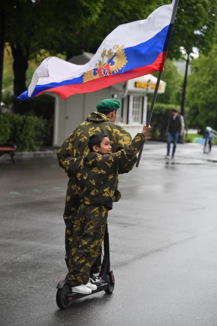 Москва. Молодые люди катаются на электросамокате с флагом РФ во время празднования Дня пограничника в Парке Горького.