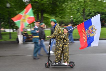 Москва. Молодые люди катаются на электросамокате с флагом РФ во время празднования Дня пограничника в Парке Горького.