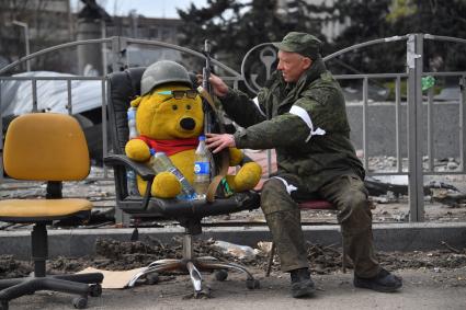 Донецкая область. г.Мариуполь. Военнослужащий ДНР сидит вместе с игрушечным медведем на улице.