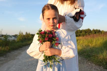 Калуга.  Женщина с девочкой в русских  народных костюмах собирают букет полевых цветов перед началом празднования  Купалы (летнее солнцестояние) в Славянском центре `Красотынка`.