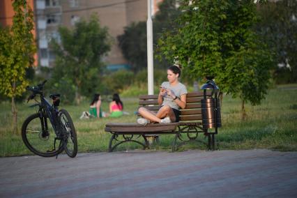 Москва. Природно-исторический парк `Косинский`. Девушка сидит на скамейке с мобильным телефоном.