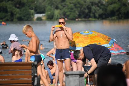 Москва. Мужчина ест кукурузу на пляже Косинского озера.