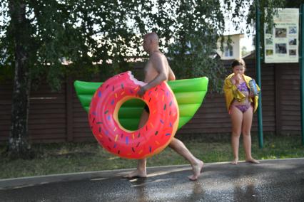 Москва. Мужчина с надувным кругом в виде пончика идет на пляже Косинского озера.