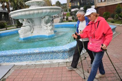 Сочи. Мужчина и женщина занимается скандинавской ходьбой на городской набережной.