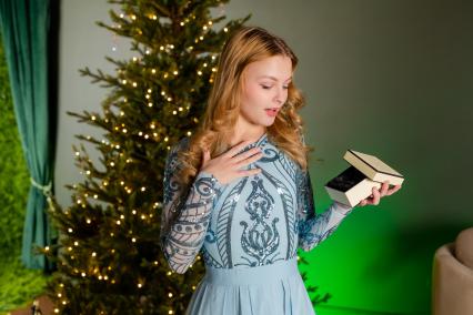 Красноярск. Девушка открывает коробку с новогодним подарком у елки.