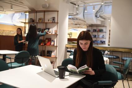 Москва. Девушка с ноутбуком и книгой сидит за столиком в бизнес-кластере на территории нового пространства `Депо. Три вокзала`на Новорязанской улице.
