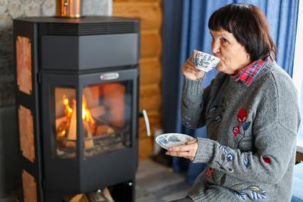 Красноярск. Пожилая женщина пьет чай у камина в своем загородном доме.