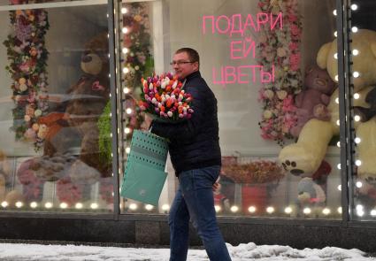 Москва. Мужчина с букетом  цветов у  витрины магазина  в международный женский день 8 Марта.