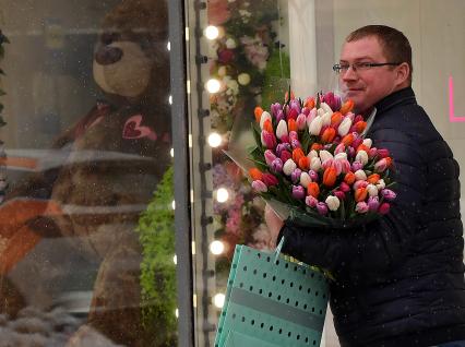 Москва. Мужчина с букетом  цветов у  витрины магазина  в международный женский день 8 Марта.