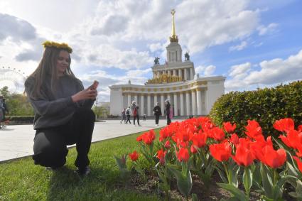 Москва. Девушка фотографирует на мобильный телефон тюльпаны рядом с павильоном #1 `Центральный` на ВДНХ.