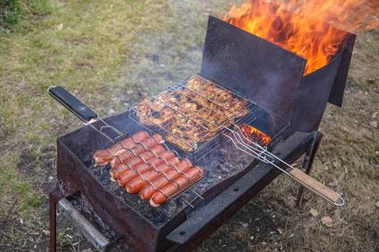 Красноярск. Приготовление куриных крылышек и сосисок на решетке на приусадебном участке.