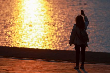 Красноярск. Девушка делает селфи на набережной во время заката.