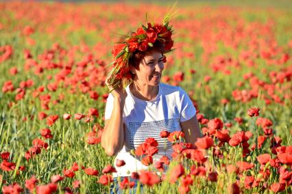 Крым. Женщина с венком из маков на голове сидит в цветущем маковом поле.