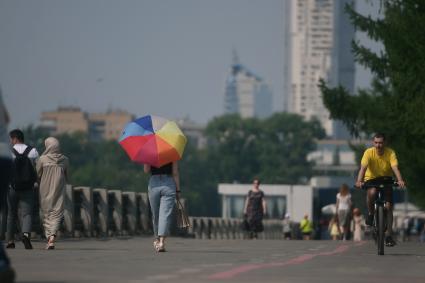 Екатеринбург. Девушка с разноцветным зонтом идет по плотинке, во время жары