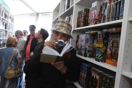 Москва. Мужчина с лупой читает книгу на IX ежегодном книжном фестивале `Красная площадь`.