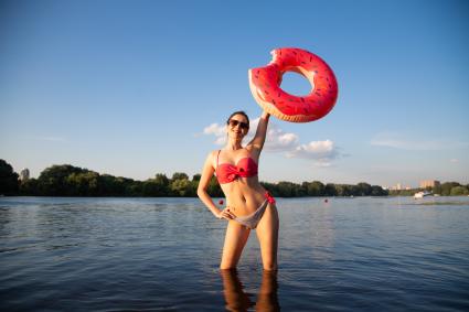 Москва. Девушка стоит в реке с надувным кругом в виде пончика на пляже Серебряный бор № 2.