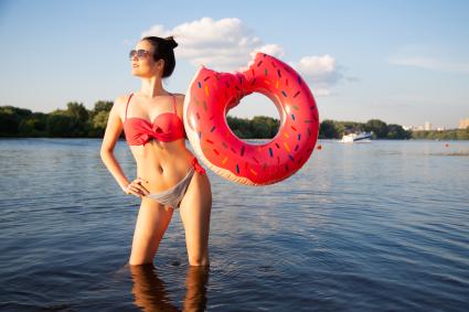 Москва. Девушка стоит в реке с надувным кругом в виде пончика на пляже Серебряный бор № 2.