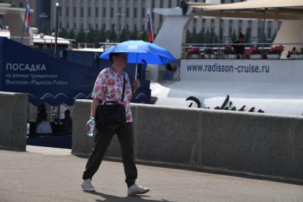 Москва. Женщина с бутылкой воды и под зонтиком идет по улице.