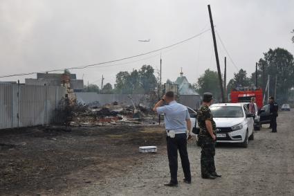 Свердловская область. Сотрудники полиции и следственного комитета у сгоревшего дома в селе Шайдуриха, в котором из-за лесного пожара перекинувшегося на дома, огнем было уничтожено 40 построек и погиб 1 человек. В небе самолет БЕ-200 Мчс России