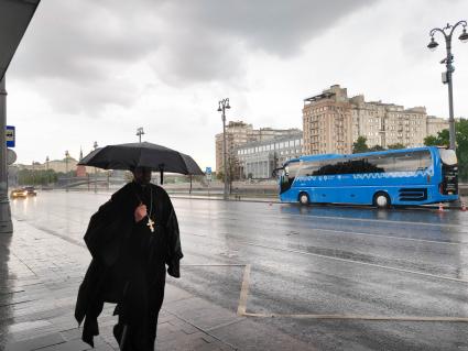 Москва. Священнослужитель с зонтом во время дождя на Пречистенской набережной.