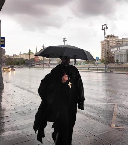 Москва. Священнослужитель с зонтом во время дождя на Пречистенской набережной.