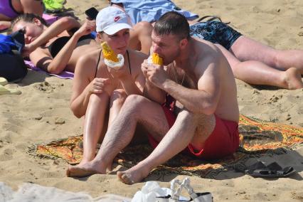 Москва. Женщина и мужчина едят горячую кукурузу на пляже озера Белое в районе Косино-Ухтомское.