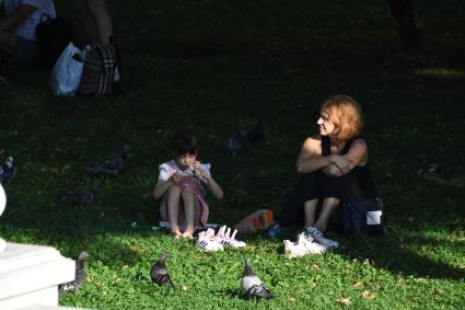 Москва.   Женщина с девочкой  сидят на газоне в парке.