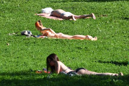 Москва.   Девушки загорают на газоне в парке.