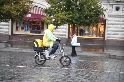 Москва.  Сотрудник службы доставки на Красной площади во время дождя.
