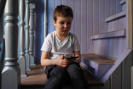 Самара. Мальчик с мобильным телефоном сидит на лестнице в доме.
