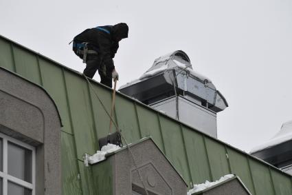 Москва. Сотрудник коммунальной службы счищает снег с крыши  дома после снегопада снегопада.