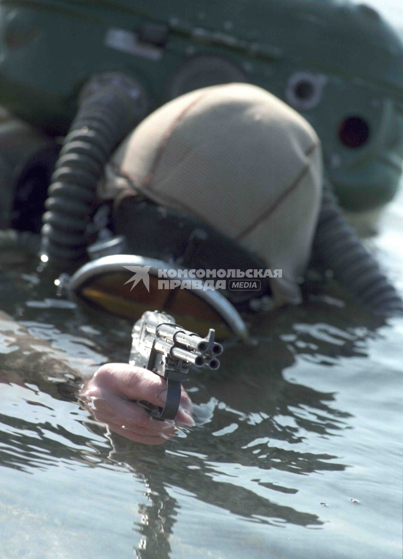 Водолаз выныривает из воды, в руках у него подводный пистолет с четырьмя стволами.