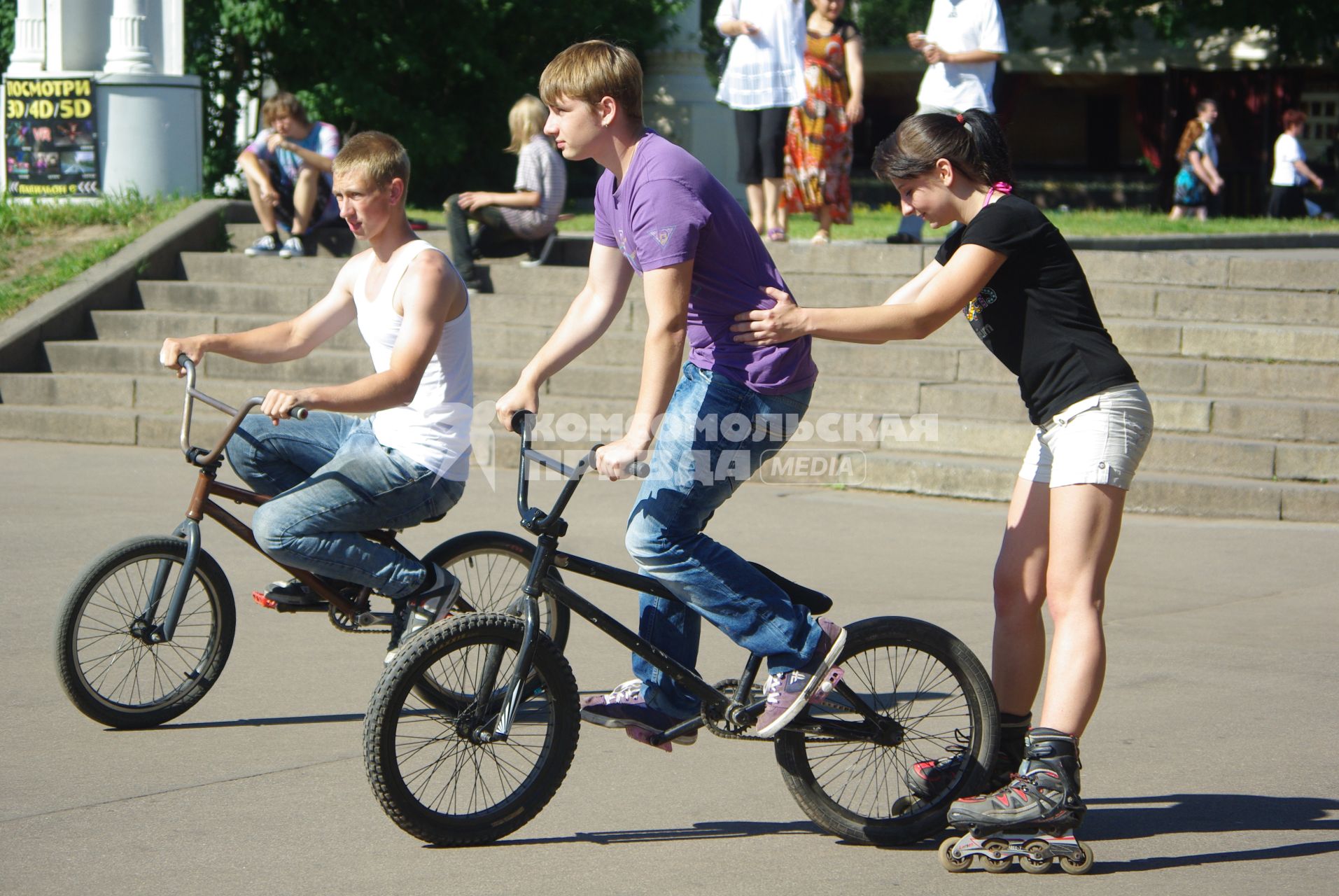 Молодые люди катаются  на велосипедах и роликах, 29 июня 2010 года.  Лето. Зной. ВВЦ (ВДНХ). Отдых. Летние развлечения. Ролики. Велосипеды. Молодежь. Парень и девушка.