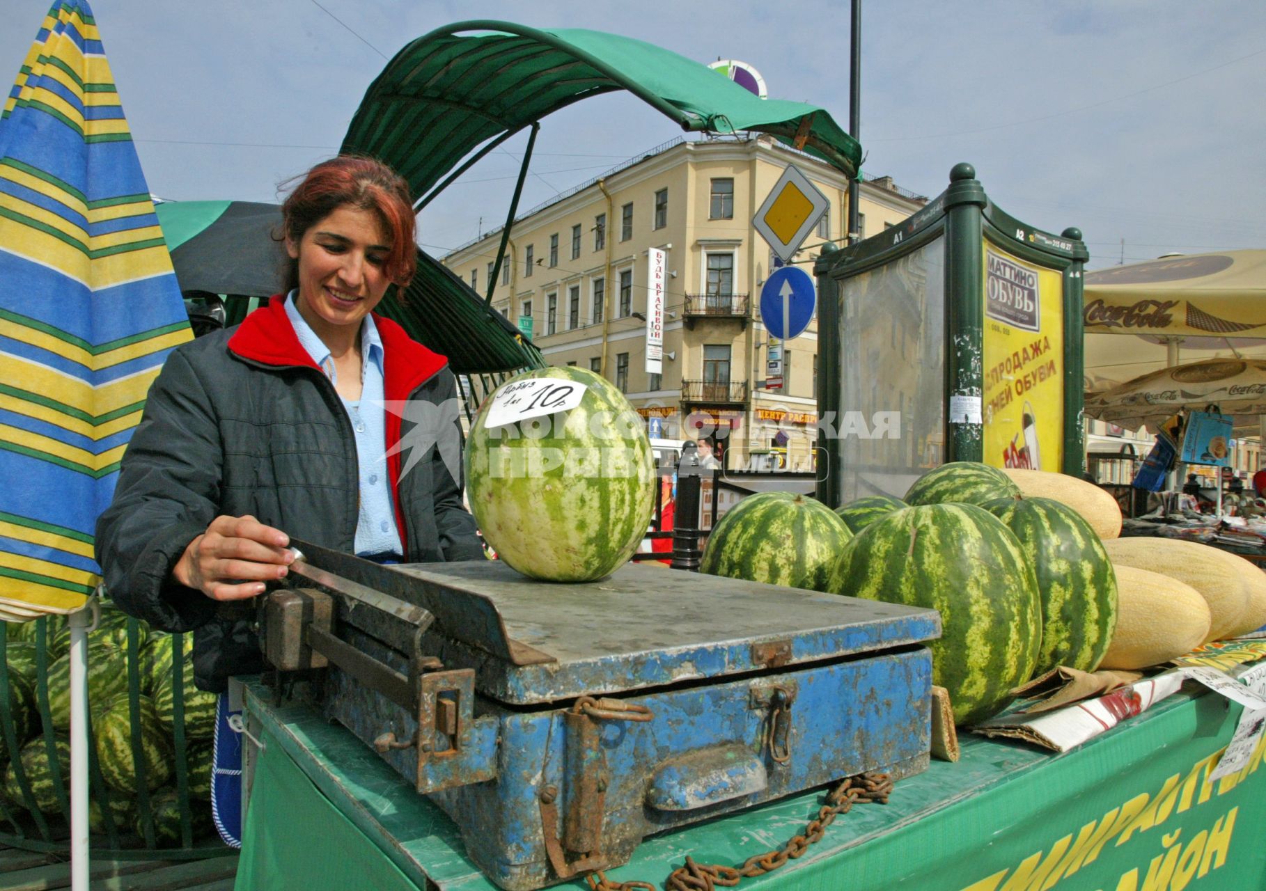 Уличная торговля арбузами. Продавец взвешивает арбуз на весах.