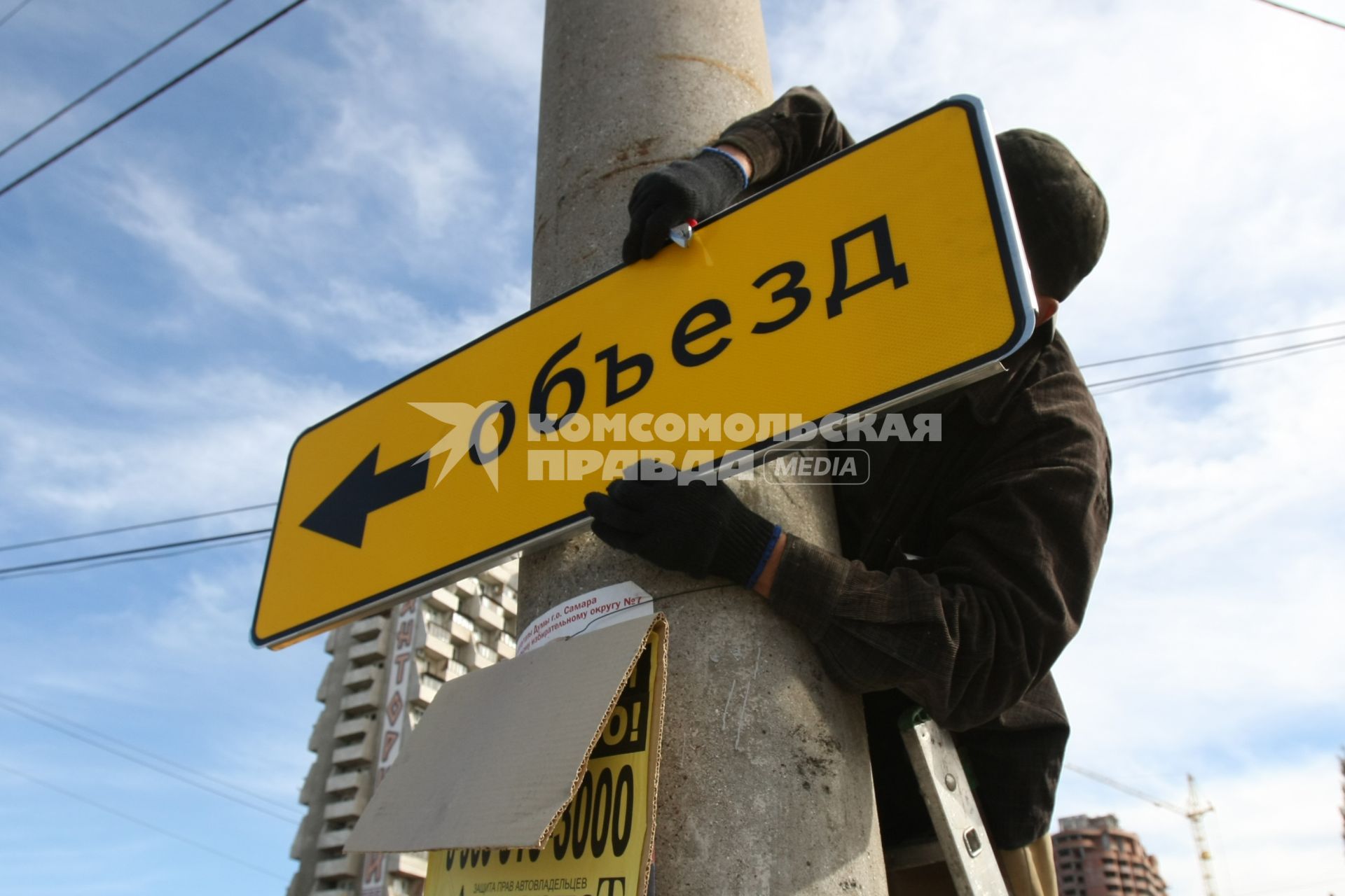 08.09.2010 Самара, Россия. Рабочий дорожной службы вешает на столб знак Объезд.