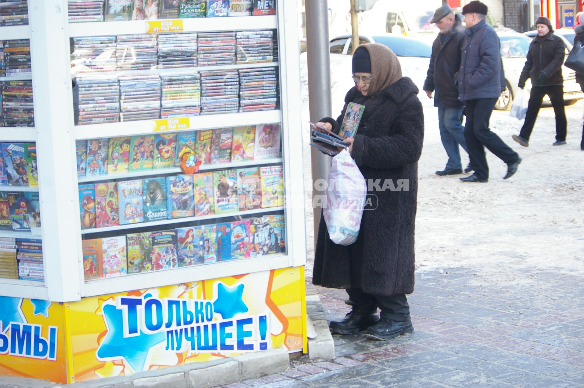 Бабулька в пуховом платке у киоска с дисками выбирает компакт диск со сказками, 26 января 2010 года, Саратов. Бабушка, бабуля, внуки, подарок, сказки,нелицензионные диски, пиратство, пуховый платок, пенсия, старость, пенсионная реформа.