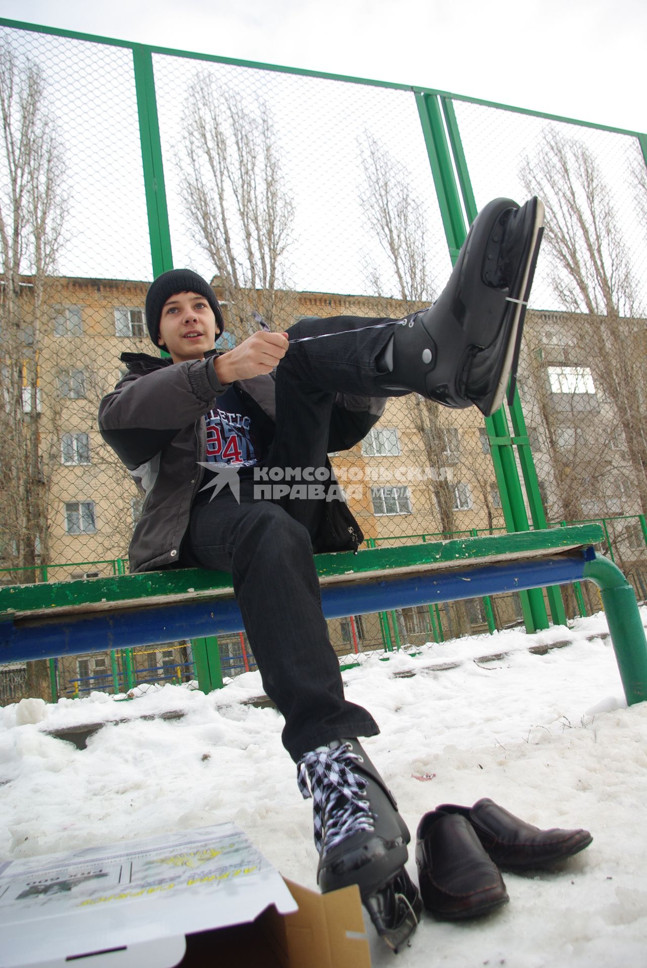 Мальчик одевает коньки сидя на лавочке перед школой, 22 декабря 2010 года, Саратов. школьники, дети, каток, коньки, зима, зимние забавы, каникулы, развлечения, отдых, школа, перемена, урок физкультуры, закалка.